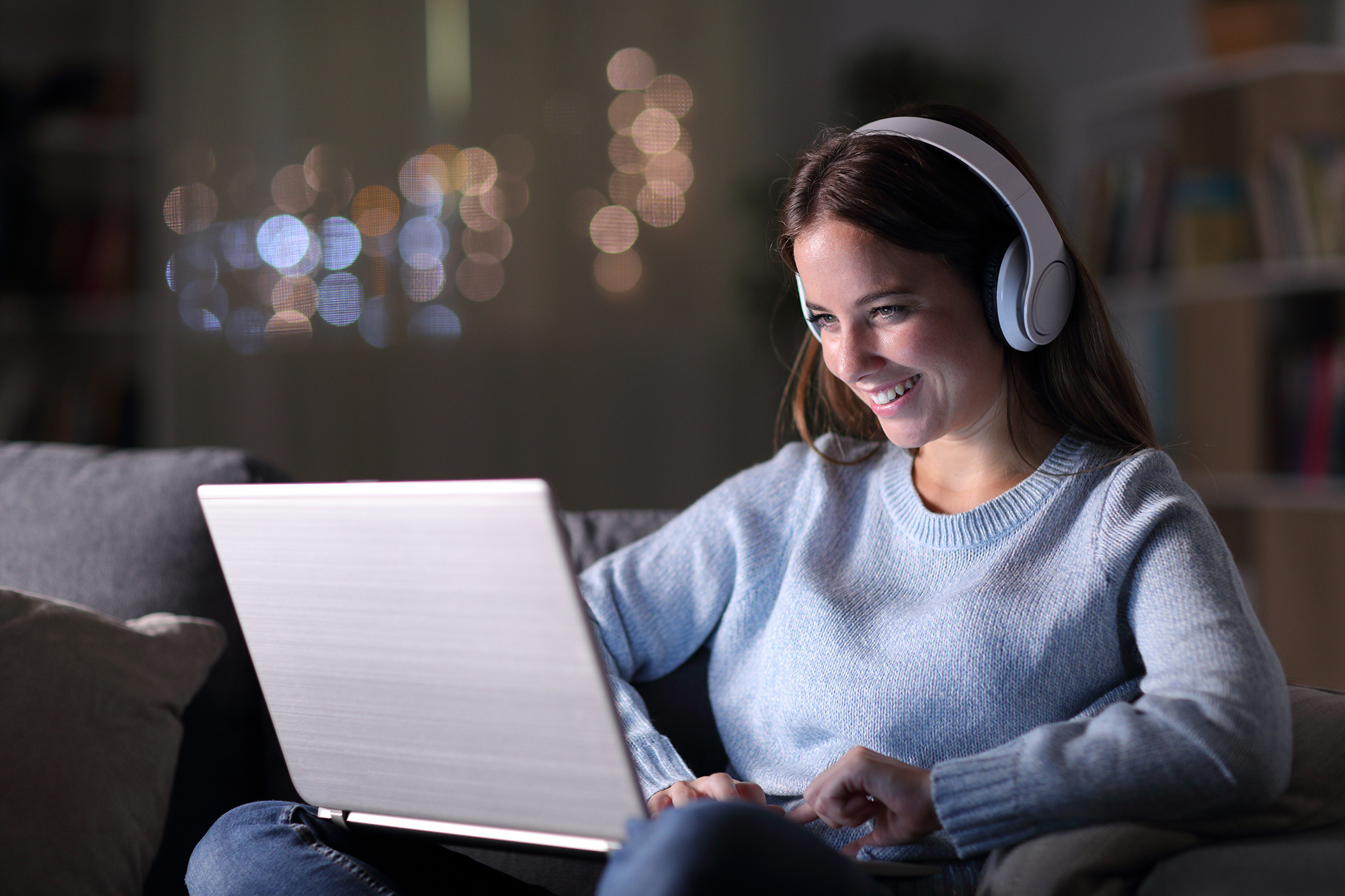 Person wearing headphones using a laptop on a sofa, with a blurred background.